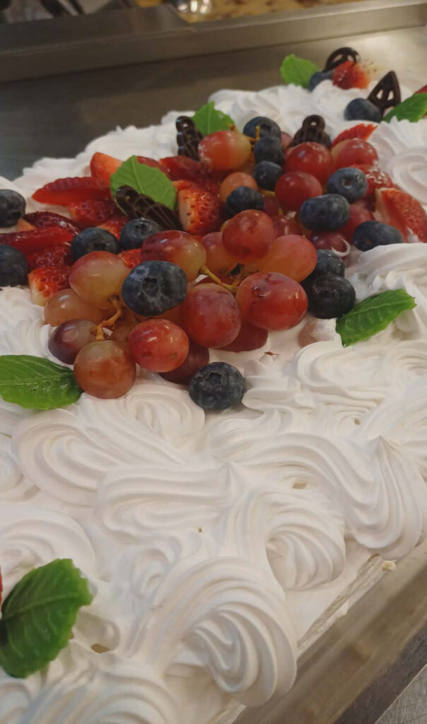 Juhlava kermakakku, joka on koristeltu runsailla tuoreilla viinirypäleillä, marjoilla ja suklaakoristeilla