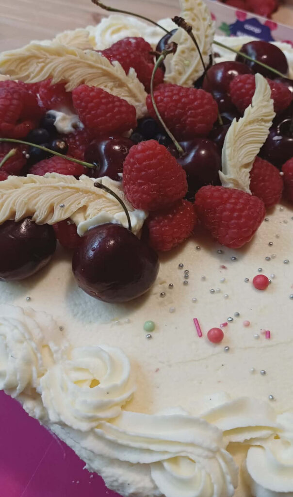 Kermainen täytekakku, joka on koristeltu tuoreilla kesämarjoilla ja valkosuklaakoristeilla