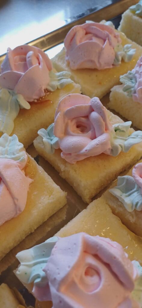 A tray of handmade retro-style mini cakes with pink buttercream roses, freshly prepared at Linda's Retro Café