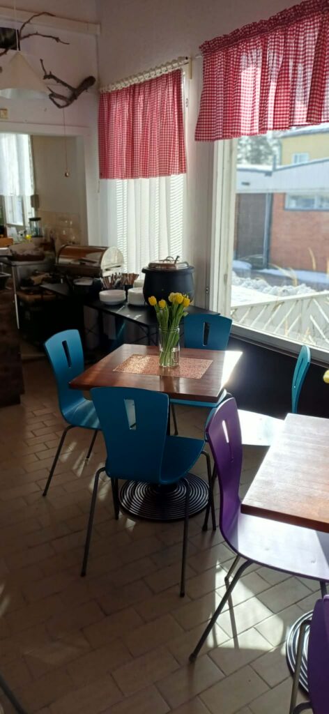 A cozy, sunlit corner of a retro-style cafeteria with colorful seating and fresh flowers on the tables